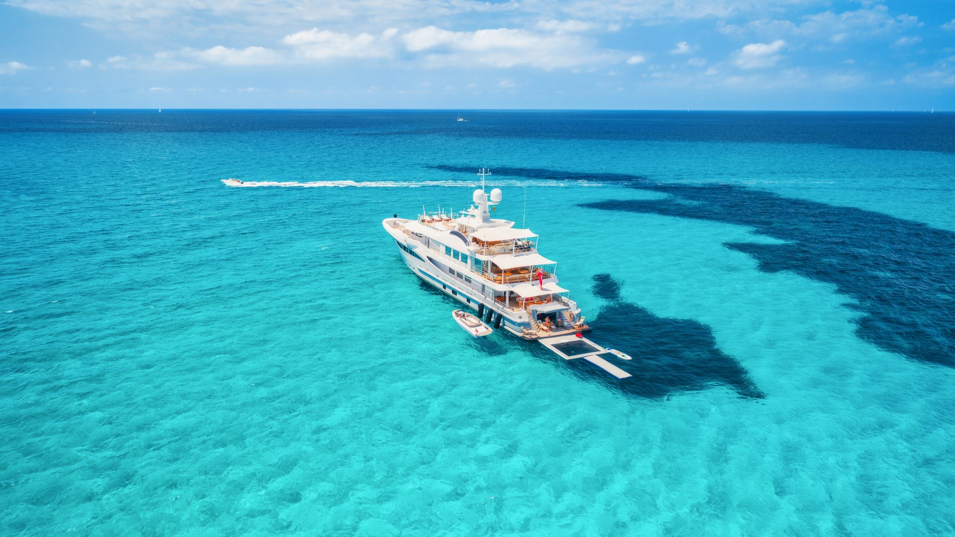 Yacht on the azure seashore in balearic islands. Aerial view of floating boat with people in transparent sea at sunny day in summer. Top view from drone. Seascape with luxury yachts in motion in bay
